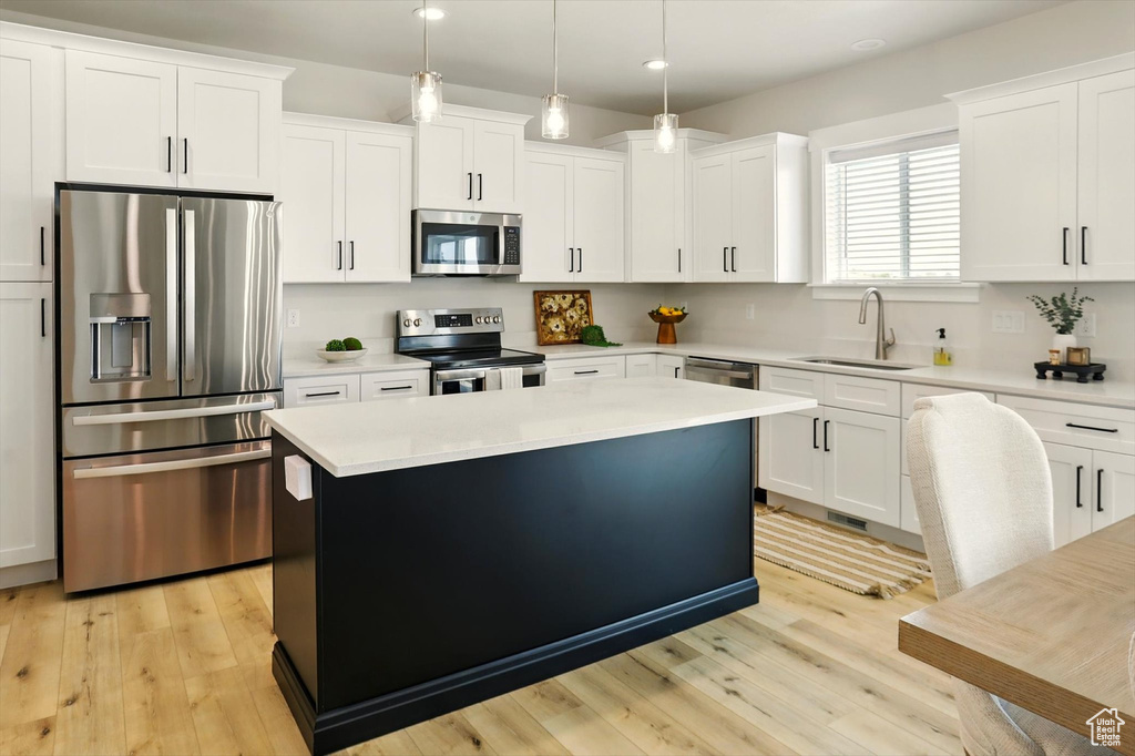 Kitchen with appliances with stainless steel finishes, a sink, recessed lighting, light wood-style flooring, and a center island