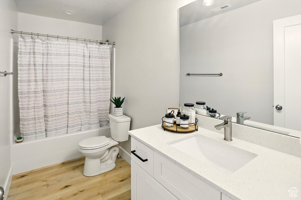 Bathroom with vanity, wood finished floors, shower / bath combination with curtain, and toilet