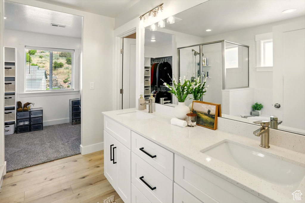 Full bathroom with a shower stall, a spacious closet, double vanity, wood finished floors, and recessed lighting