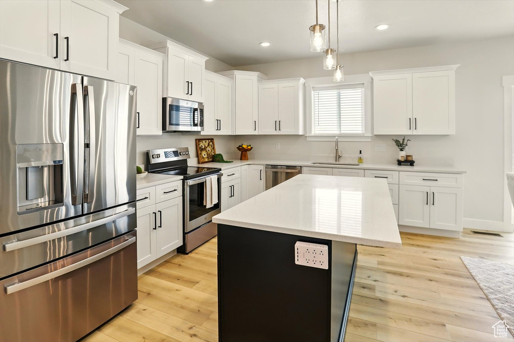 Kitchen featuring appliances with stainless steel finishes, a sink, a kitchen island, light countertops, and white cabinets