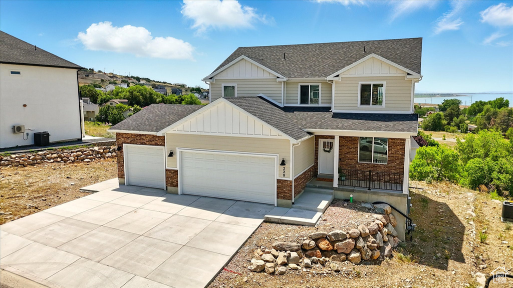 View of front facade with board and batten siding, roof with shingles, an attached garage, brick siding, and driveway