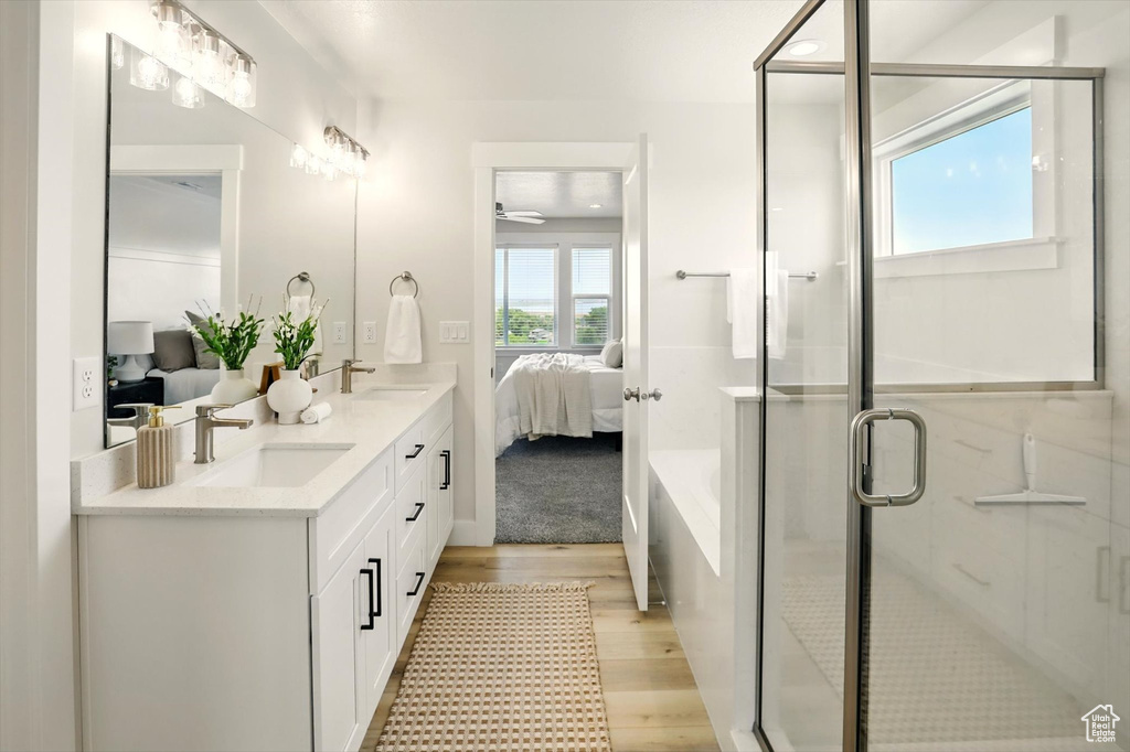 Ensuite bathroom featuring wood finished floors, double vanity, a stall shower, and a tub to relax in