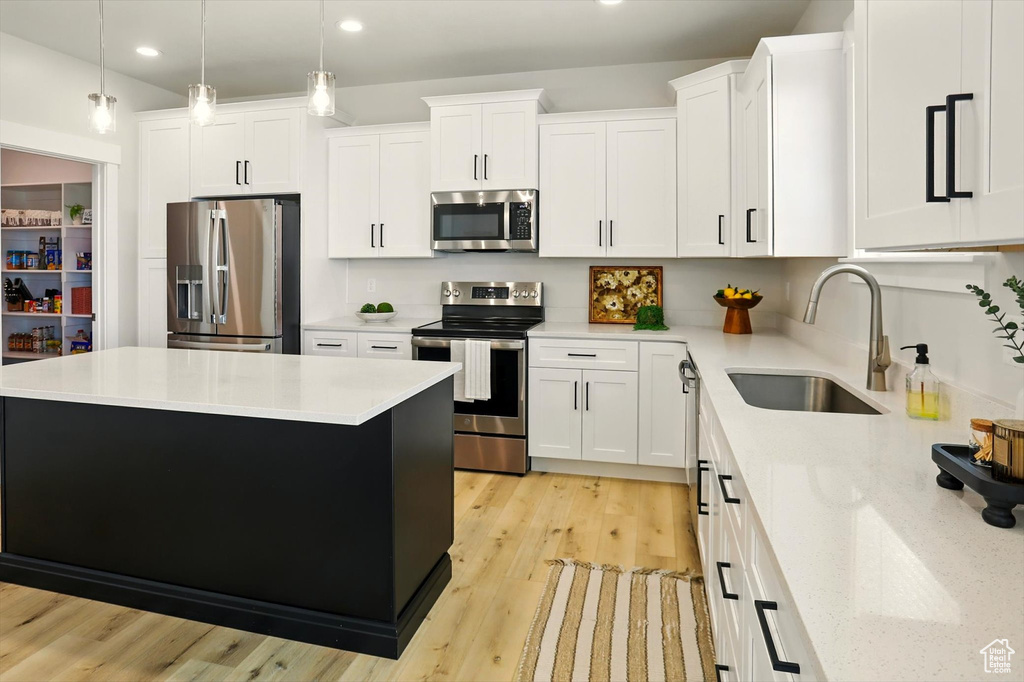 Kitchen with appliances with stainless steel finishes, a sink, recessed lighting, white cabinetry, and a center island