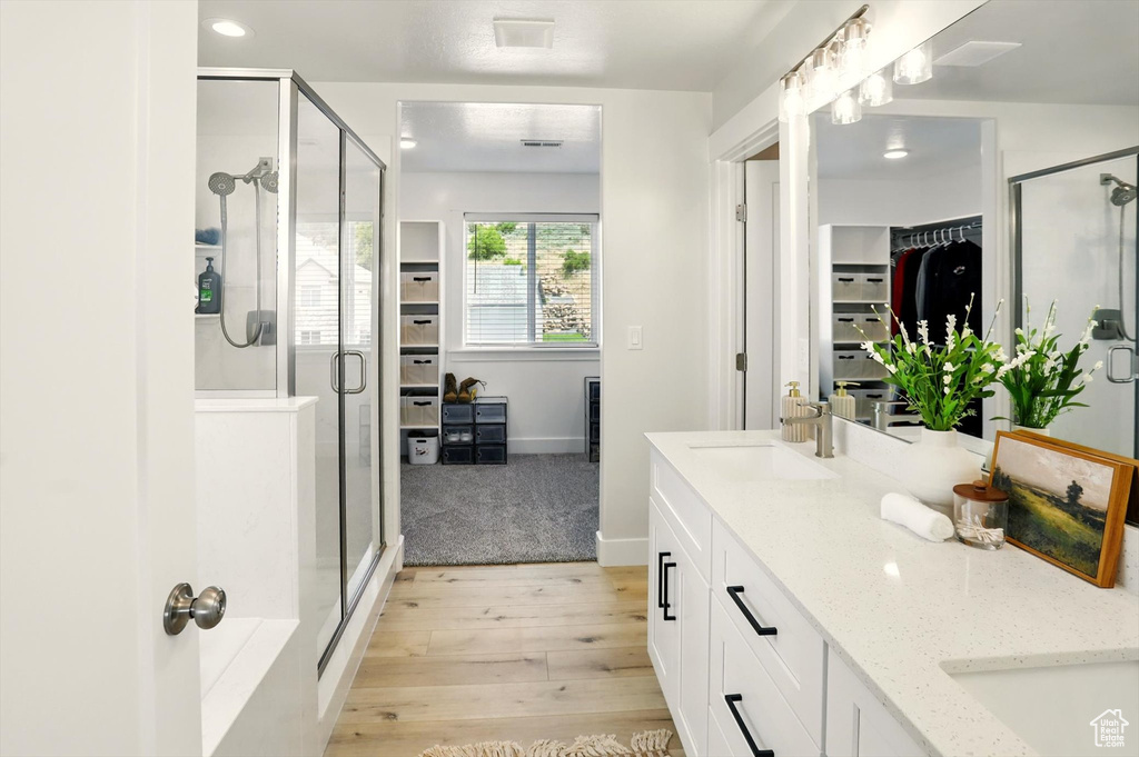 Bathroom with wood finished floors, double vanity, a shower stall, a walk in closet, and baseboards