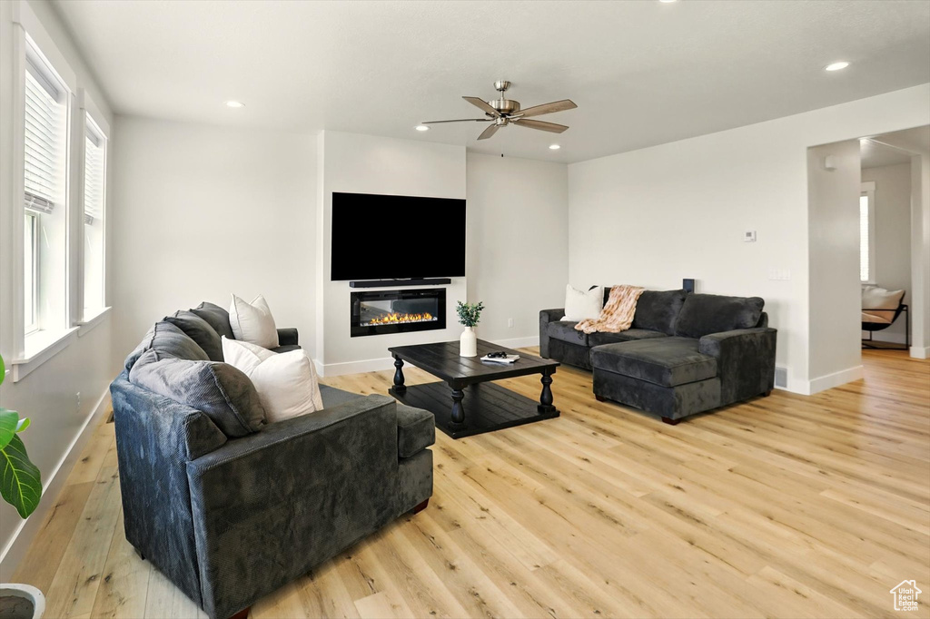 Living room with wood finished floors, recessed lighting, baseboards, a ceiling fan, and a glass covered fireplace