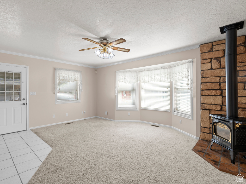 Unfurnished living room featuring a wood stove, carpet floors, a ceiling fan, crown molding, and baseboards