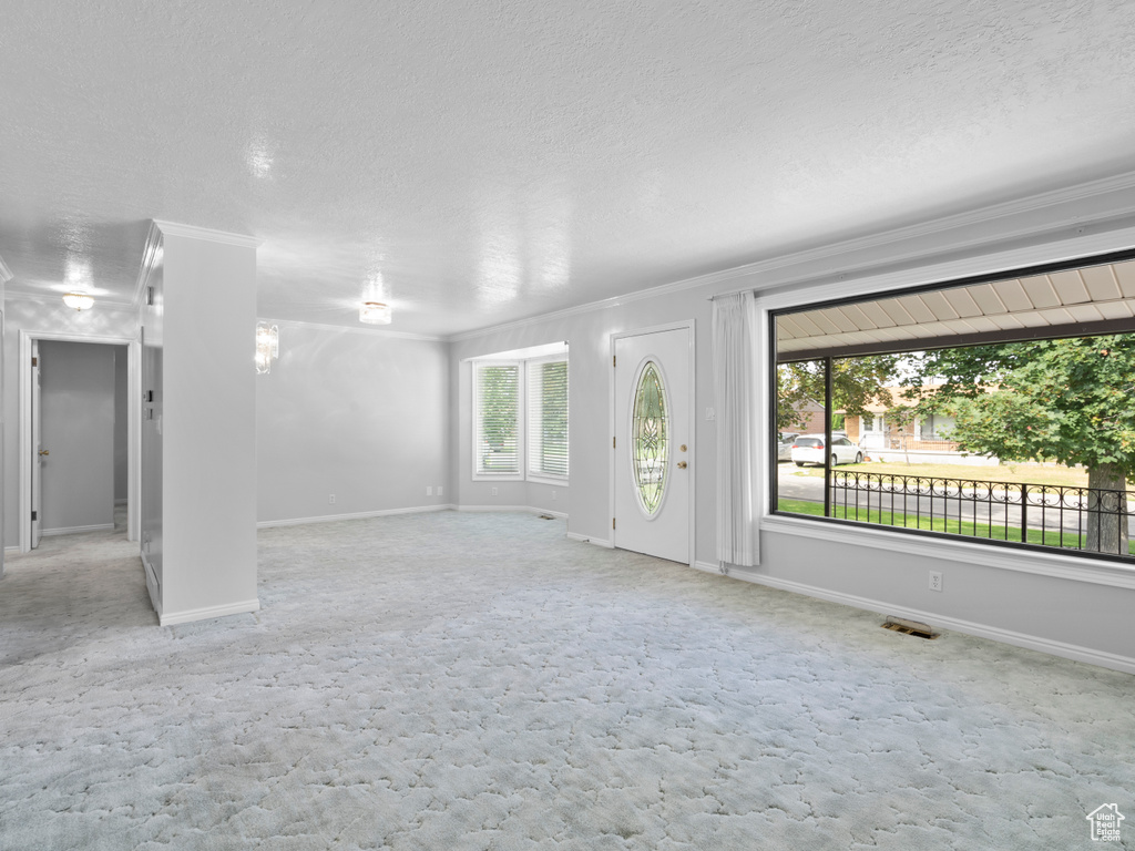 Unfurnished living room featuring crown molding, carpet, a textured ceiling, and baseboards