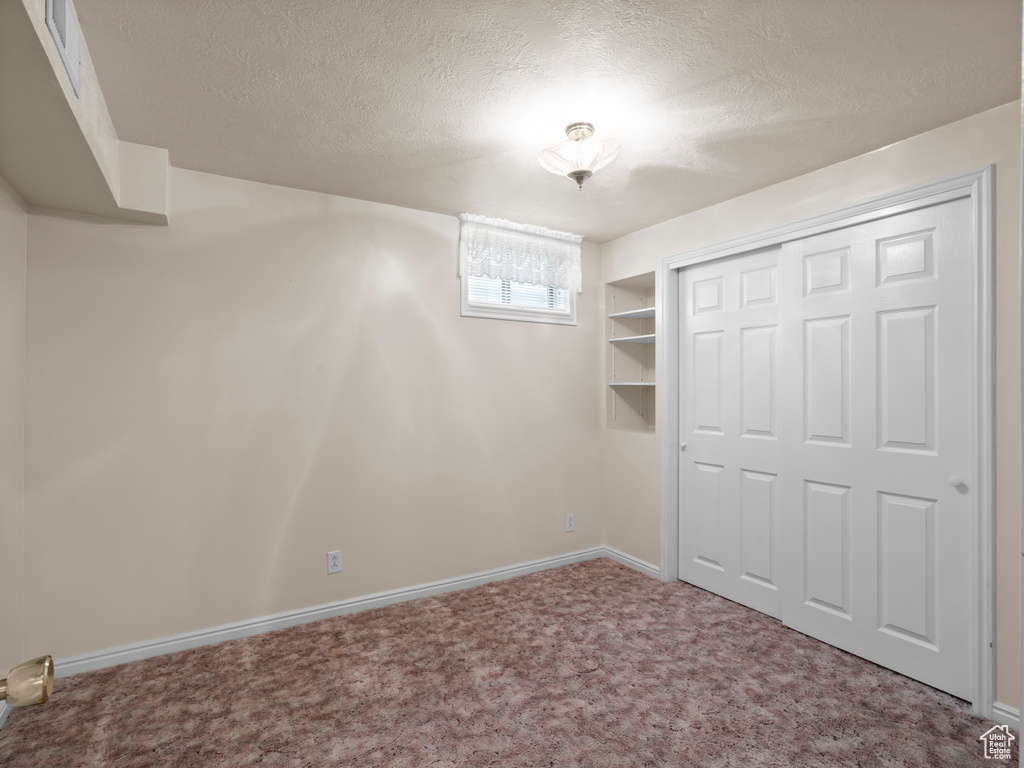 Unfurnished bedroom featuring a textured ceiling, carpet, baseboards, and a closet