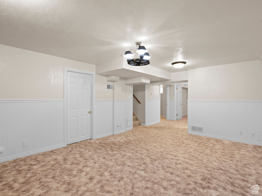 Finished basement featuring wainscoting, stairs, a textured ceiling, and light colored carpet