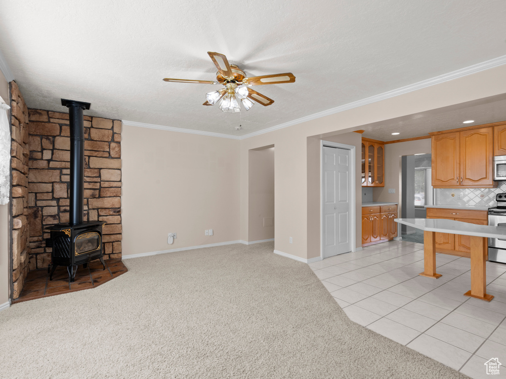 Unfurnished living room with a wood stove, ceiling fan, light colored carpet, ornamental molding, and baseboards