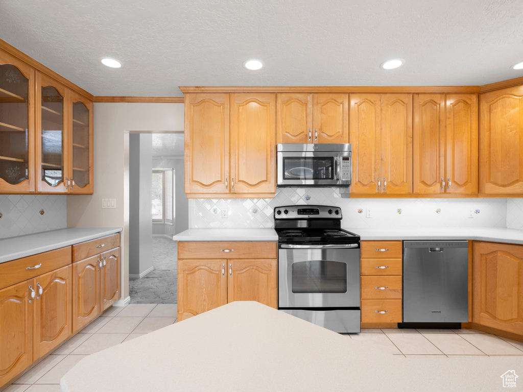 Kitchen with stainless steel appliances, light countertops, glass insert cabinets, recessed lighting, and light tile patterned flooring
