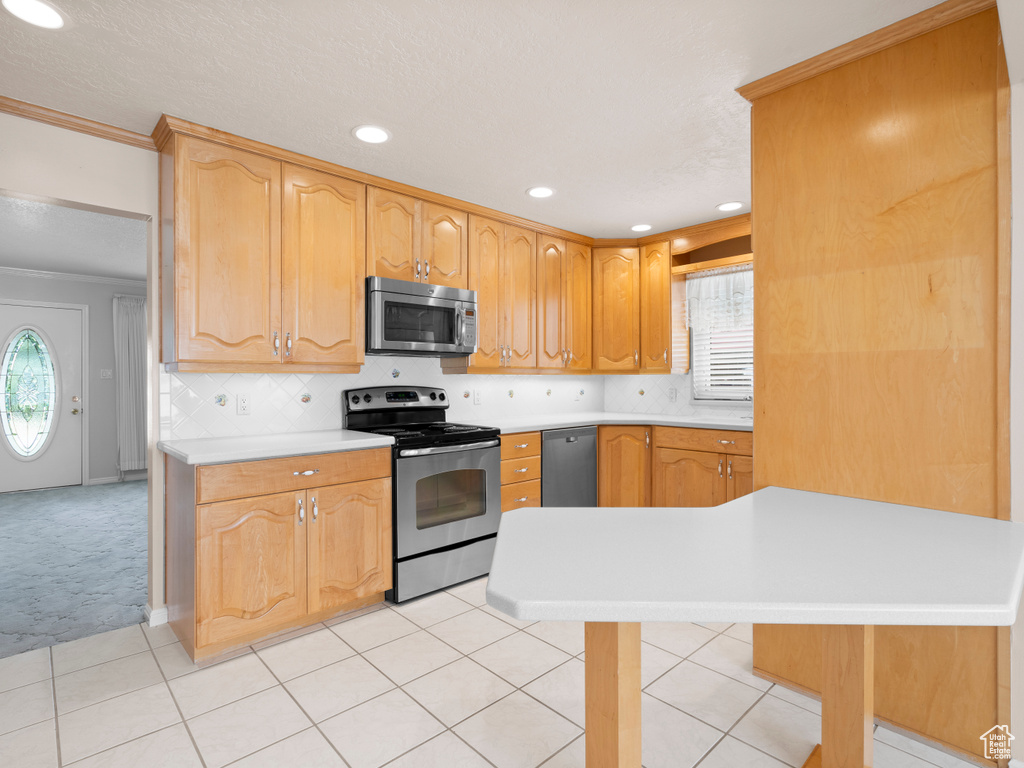 Kitchen with appliances with stainless steel finishes, ornamental molding, light countertops, light colored carpet, and light tile patterned flooring