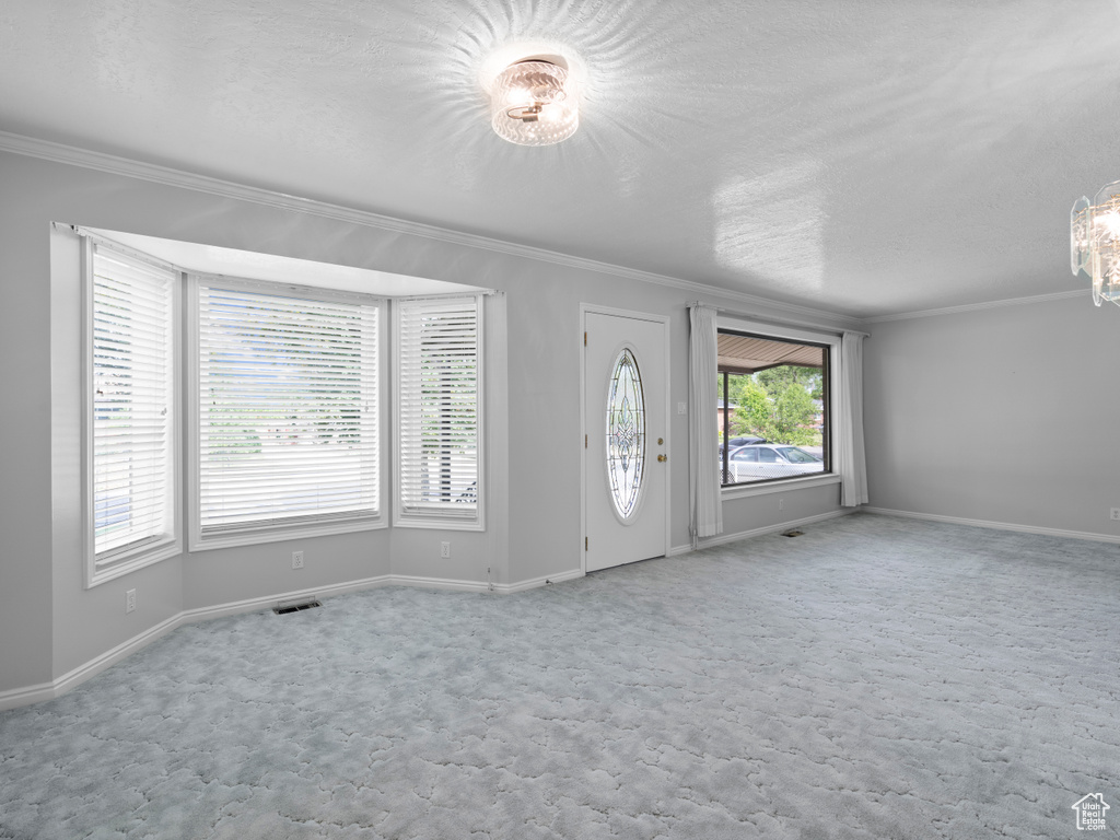 Entrance foyer featuring ornamental molding, a textured ceiling, carpet floors, and baseboards