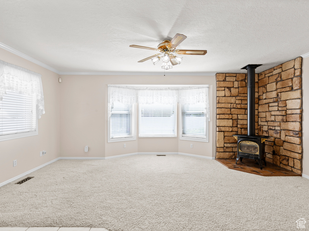 Unfurnished living room with a wood stove, ceiling fan, crown molding, carpet flooring, and baseboards