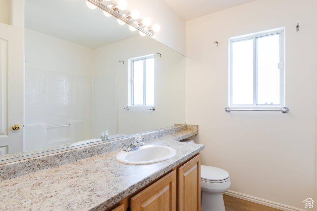 Bathroom with vanity, toilet, wood finished floors, baseboards, and a shower