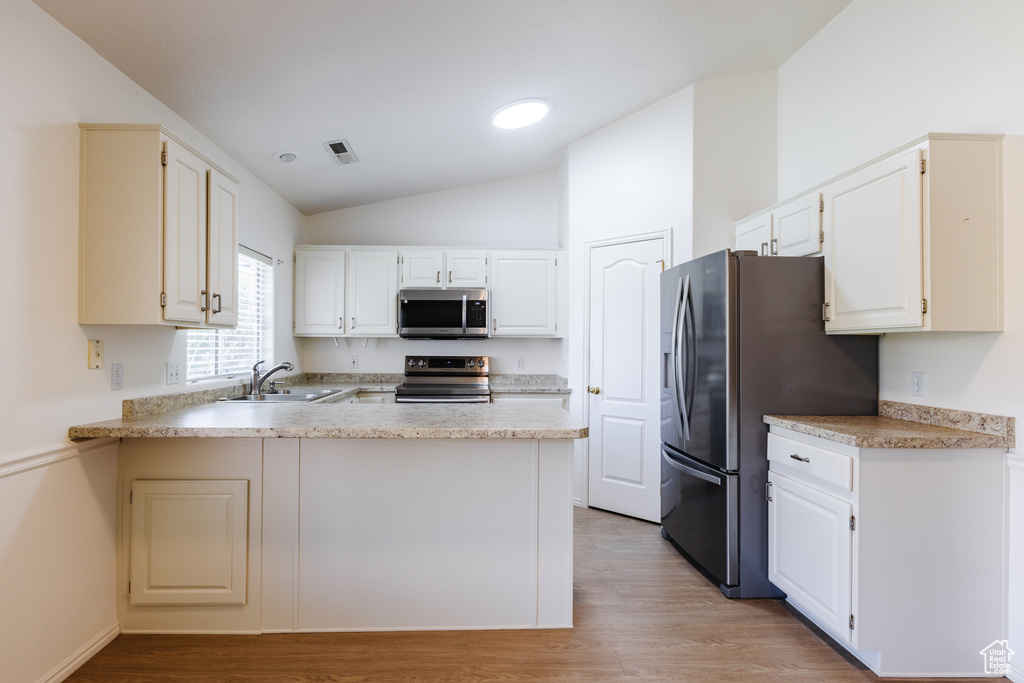 Kitchen with appliances with stainless steel finishes, a sink, lofted ceiling, a peninsula, and light wood-style flooring