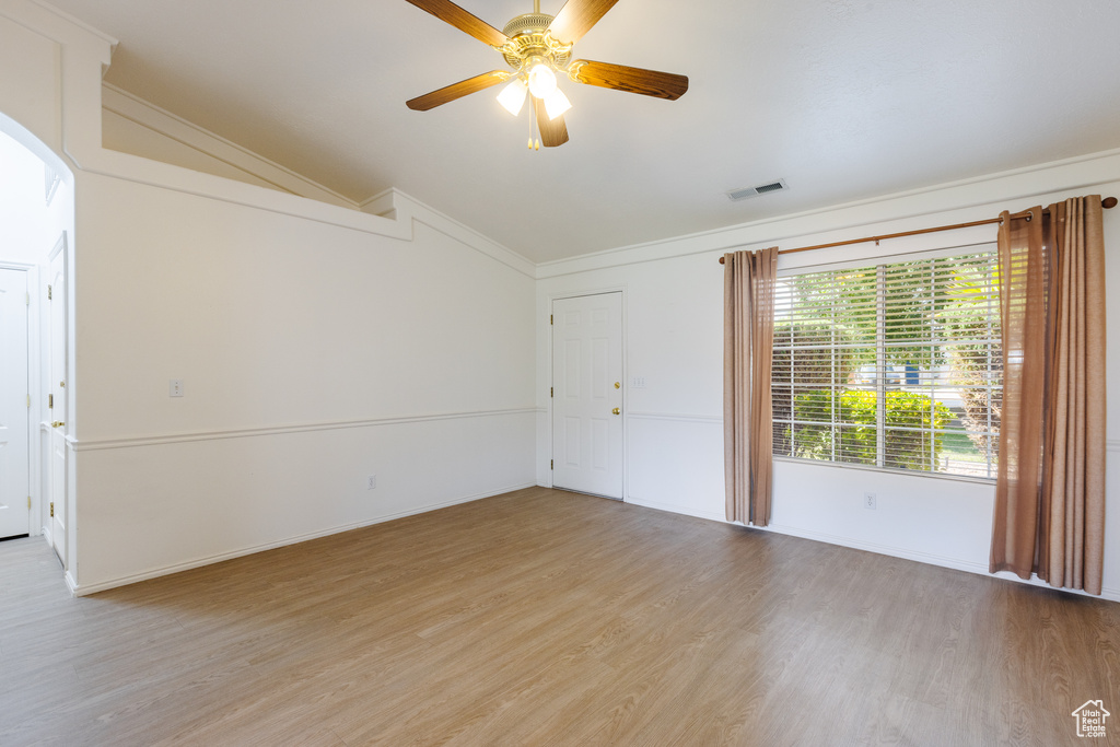 Empty room with vaulted ceiling, crown molding, light wood-style flooring, a ceiling fan, and baseboards