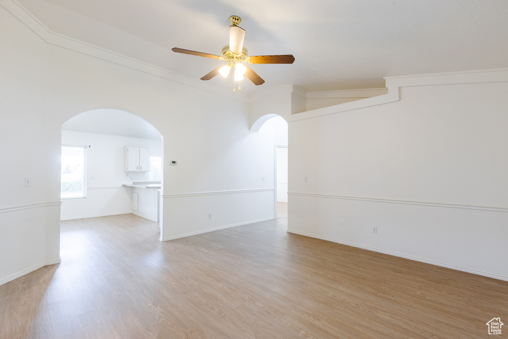 Spare room featuring arched walkways, a ceiling fan, light wood-type flooring, crown molding, and baseboards