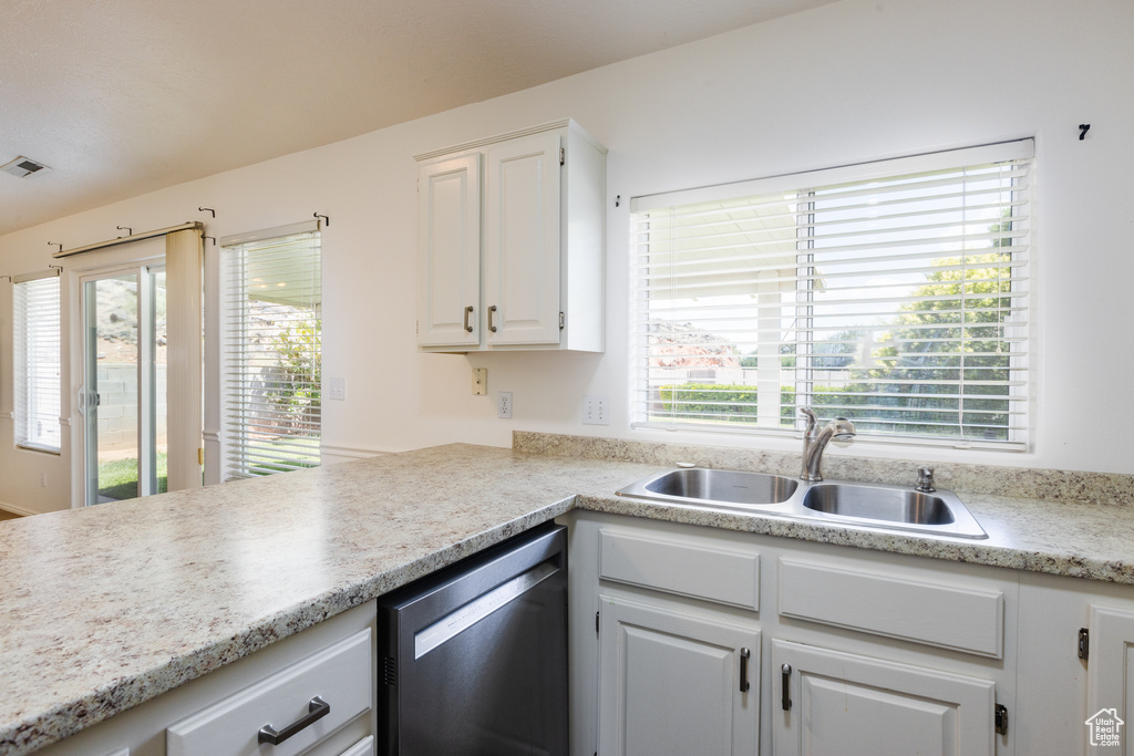 Kitchen with a sink, dishwasher, white cabinetry, and light countertops