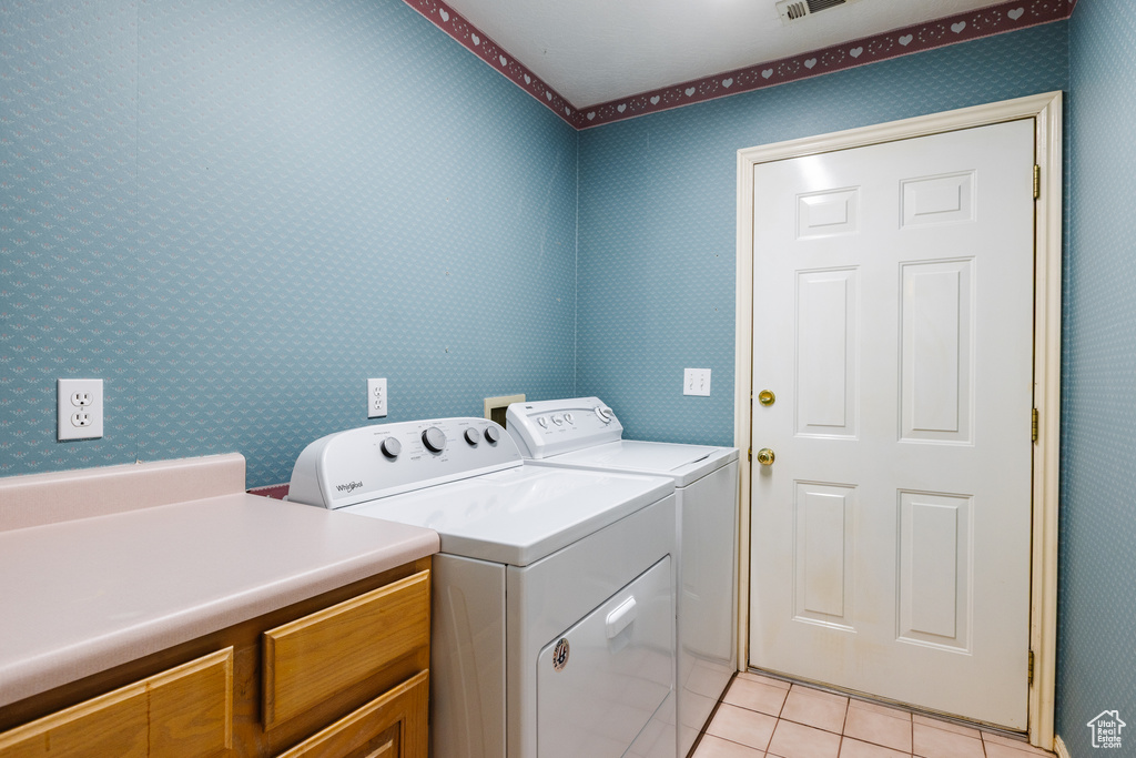 Washroom featuring washer and clothes dryer, light tile patterned floors, wallpapered walls, and cabinet space