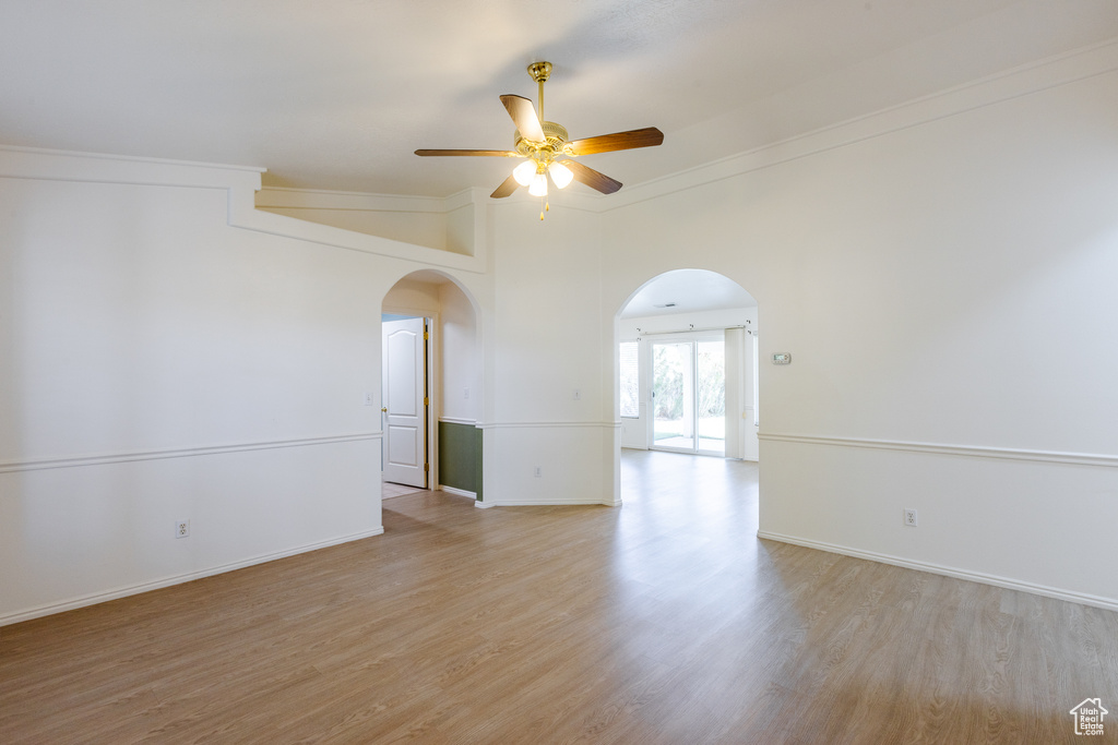 Empty room with arched walkways, a ceiling fan, light wood-style flooring, ornamental molding, and baseboards