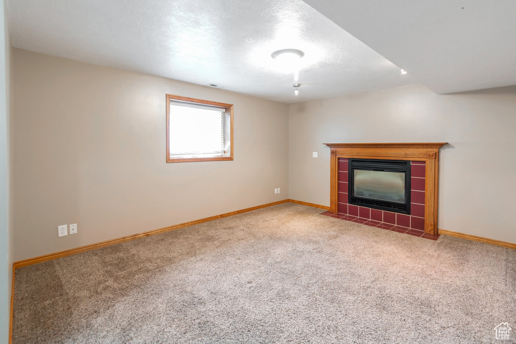 Unfurnished living room with carpet, a tiled fireplace, and a textured ceiling
