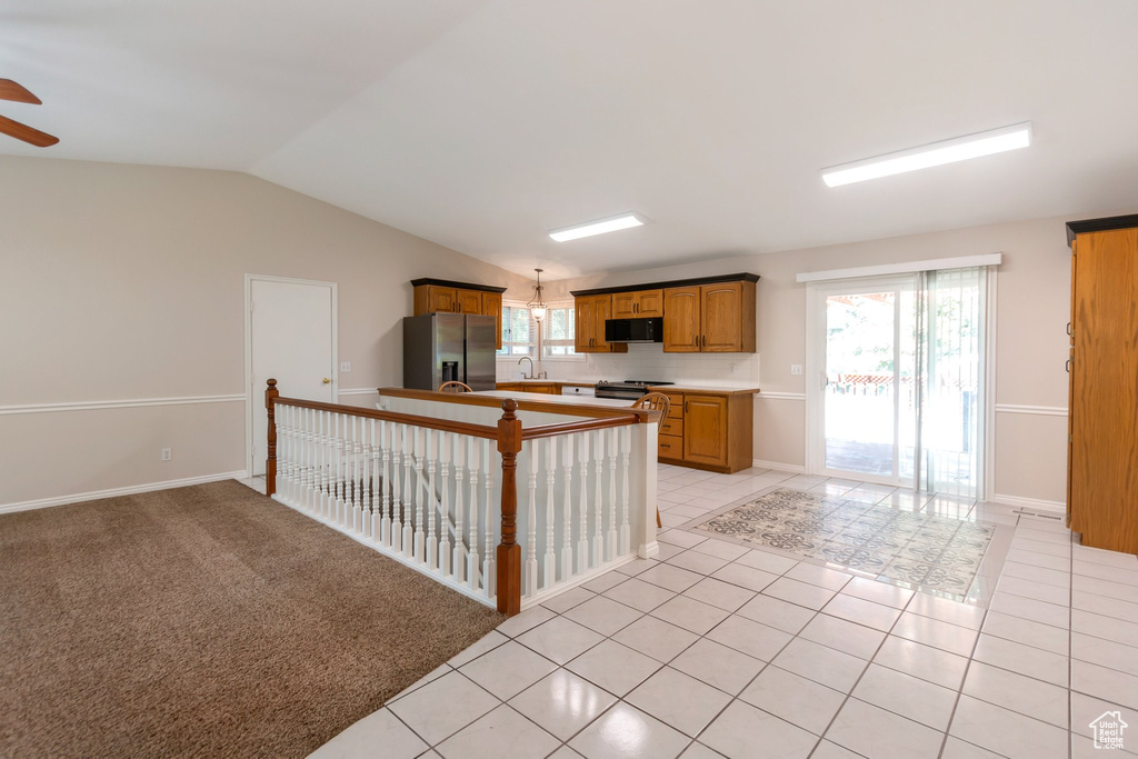 Kitchen with stainless steel fridge with ice dispenser, black microwave, range with electric cooktop, light tile patterned flooring, and lofted ceiling