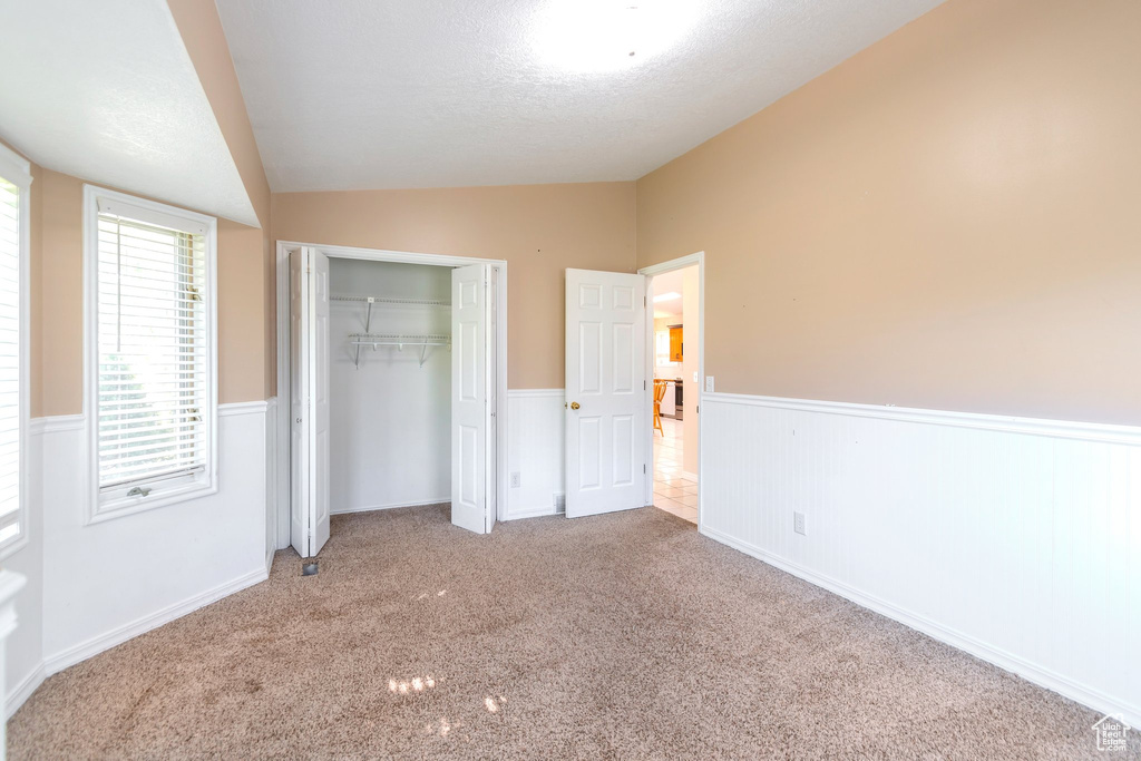 Unfurnished bedroom with lofted ceiling, wainscoting, a closet, carpet, and a textured ceiling