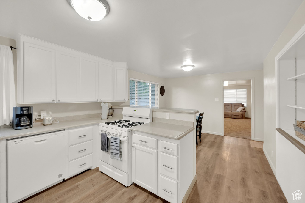 Kitchen featuring white appliances, a peninsula, white cabinets, light countertops, and light wood-style flooring