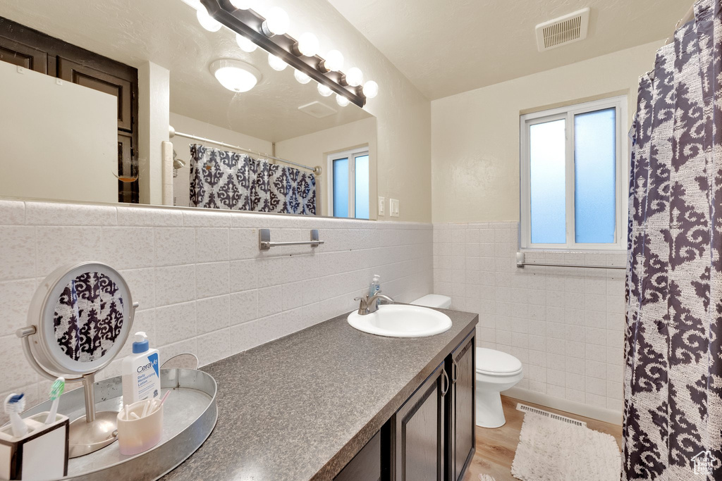Full bath with double vanity, toilet, wainscoting, tile walls, and curtained shower