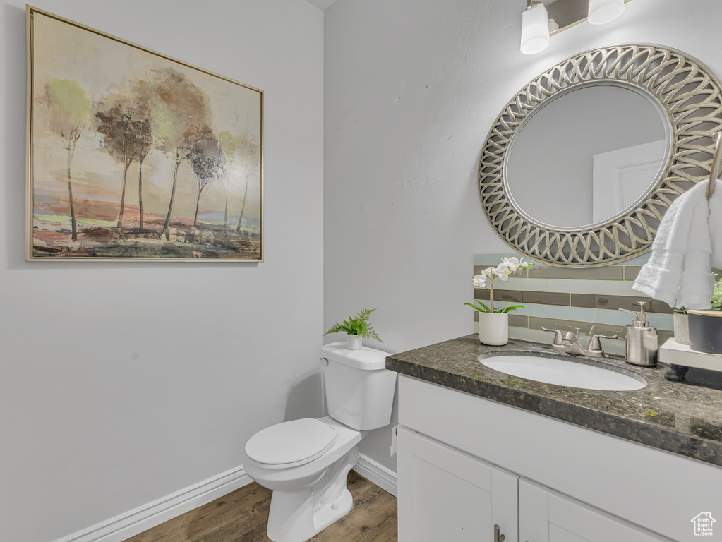 Half bathroom featuring wood finished floors, vanity, toilet, and baseboards