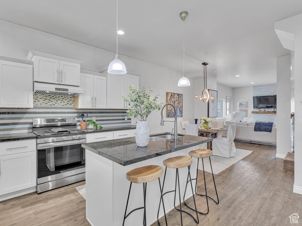 Kitchen with stainless steel gas stove, a sink, under cabinet range hood, tasteful backsplash, and white cabinetry