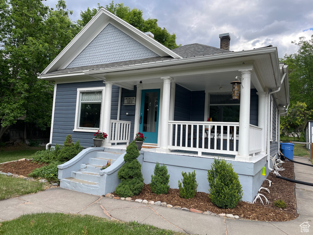 View of front of property featuring covered porch, a chimney, and a shingled roof