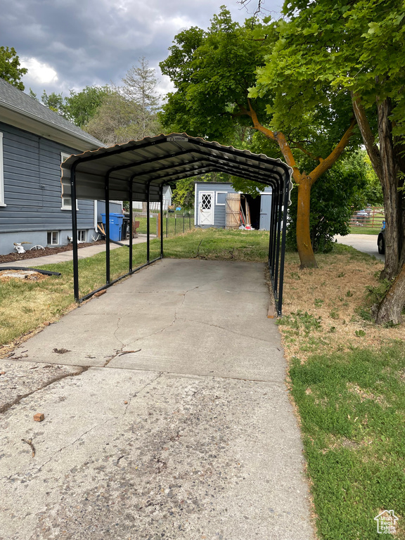 View of car parking featuring a detached carport, concrete driveway, and a shed