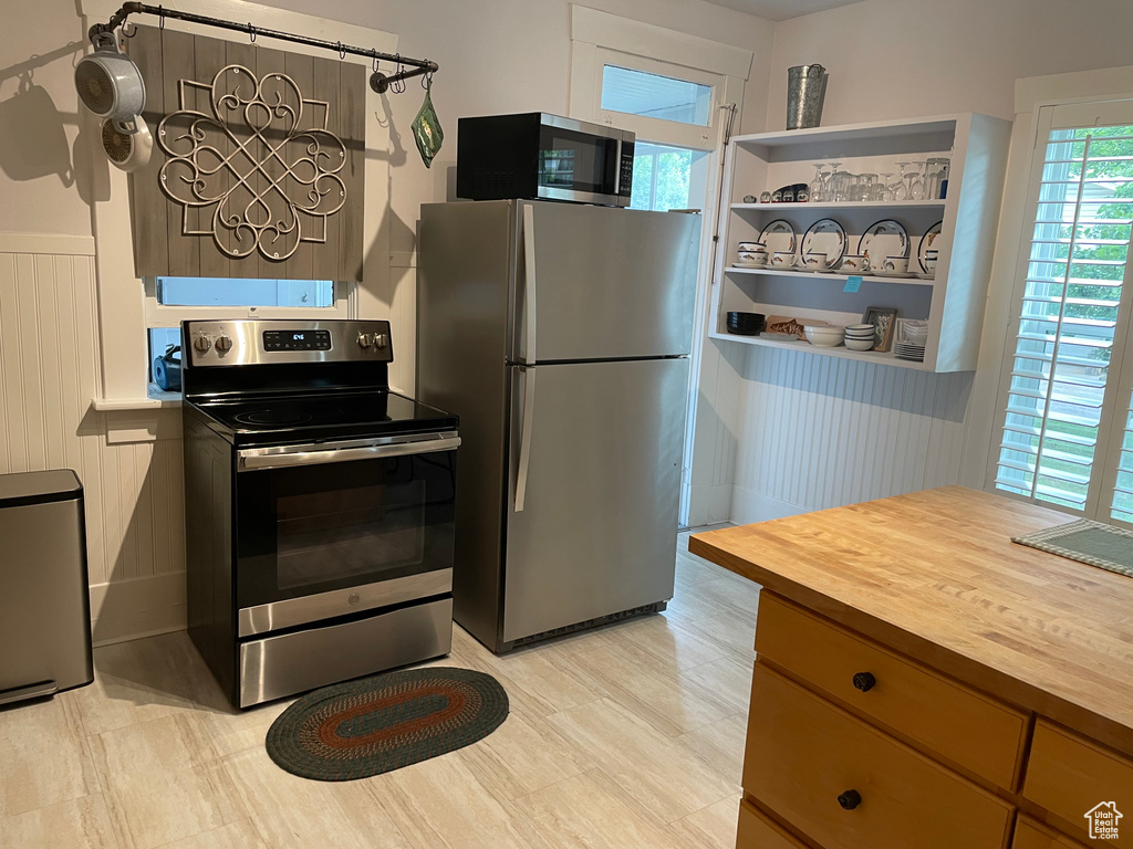 Kitchen with stainless steel appliances, wood counters, open shelves, and a wainscoted wall