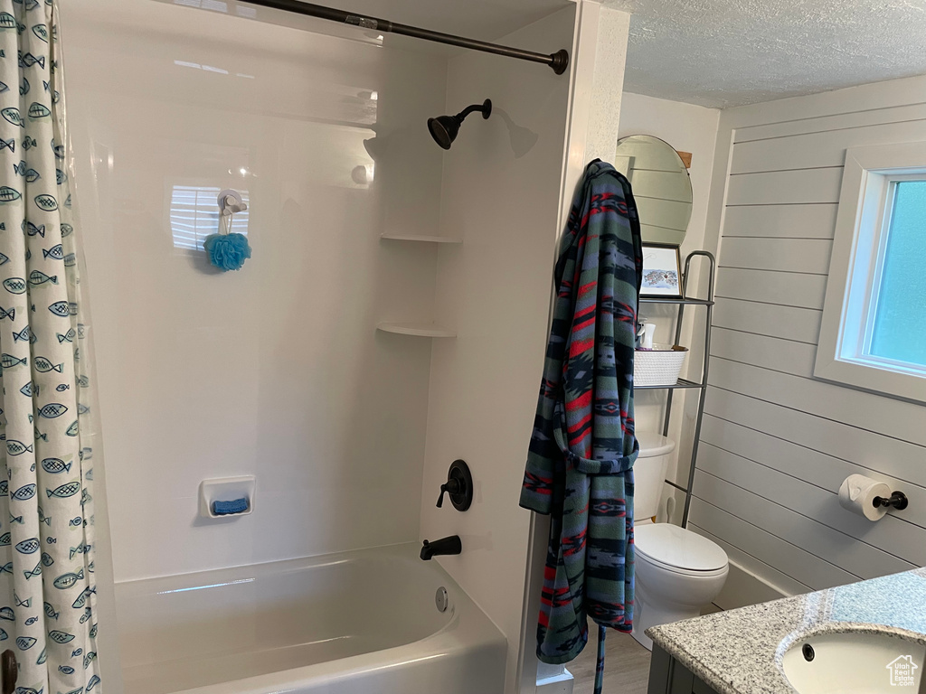 Full bathroom featuring shower / bath combination with curtain, vanity, a textured ceiling, and wood walls