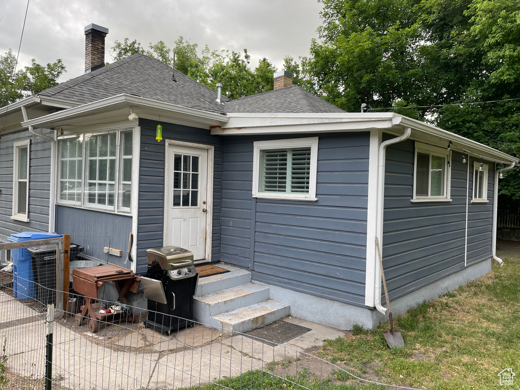 Back of property featuring entry steps, a chimney, and a shingled roof