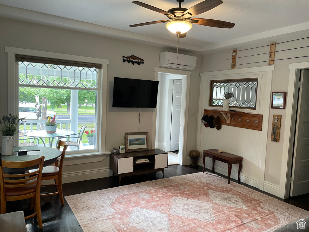 Living area with an AC wall unit, a ceiling fan, and dark wood-style floors