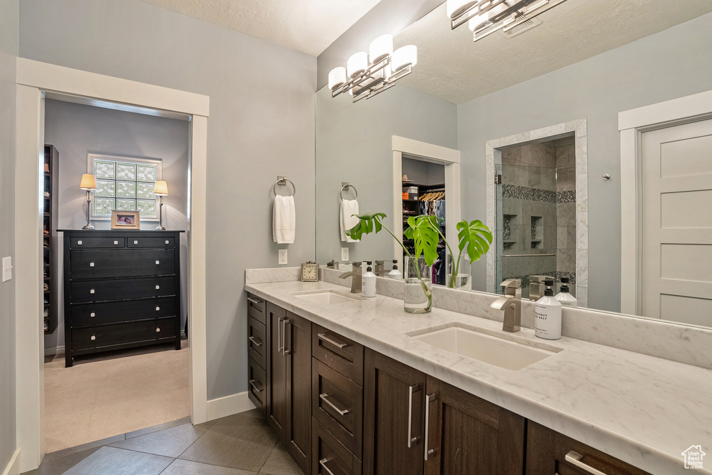 Bathroom featuring double vanity, a spacious closet, tiled shower, tile patterned floors, and baseboards