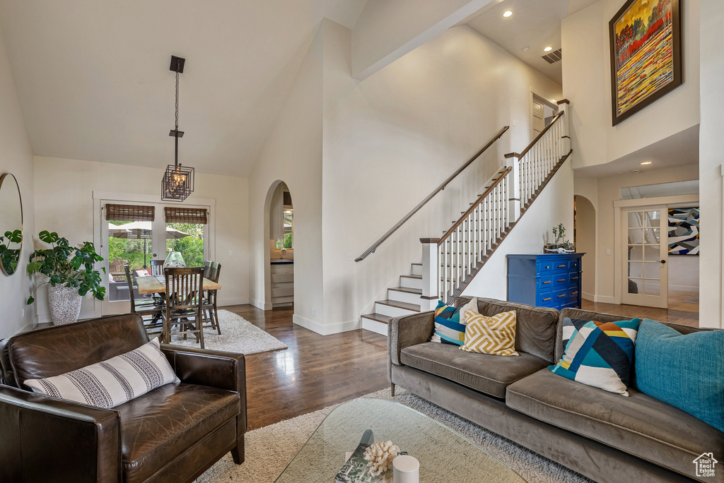 Living area with arched walkways, high vaulted ceiling, baseboards, wood finished floors, and stairs