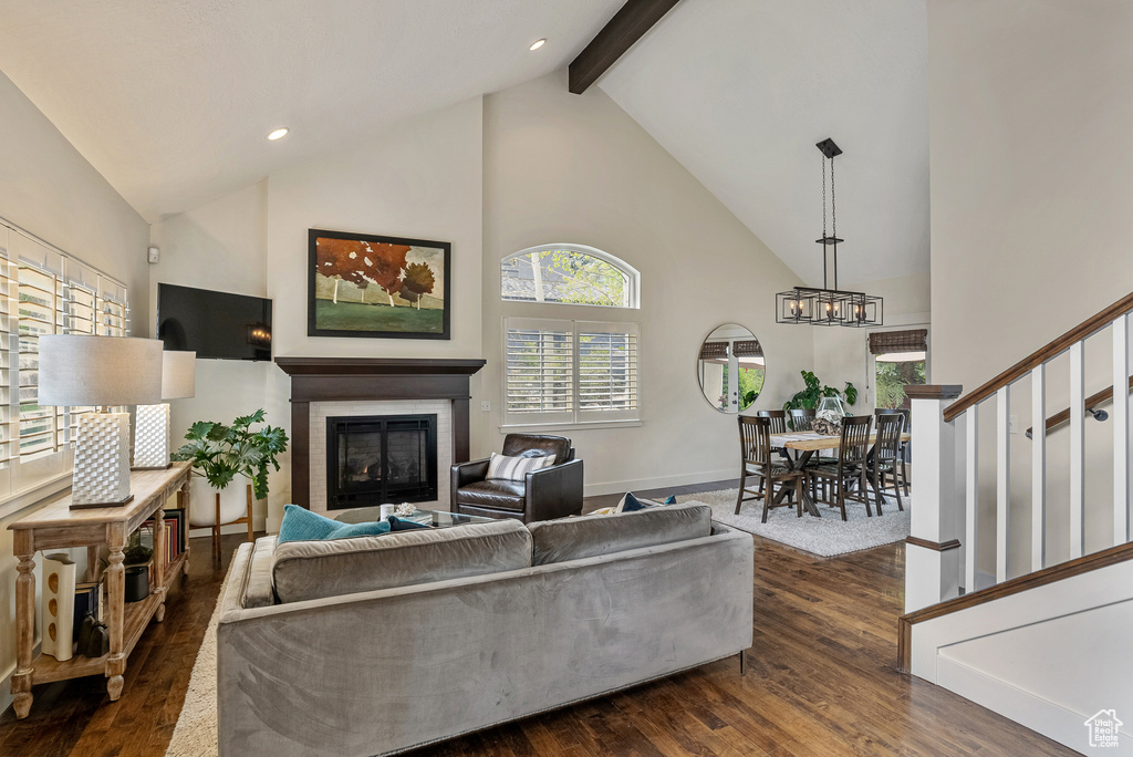 Living area with high vaulted ceiling, dark wood-style flooring, a glass covered fireplace, stairway, and beam ceiling