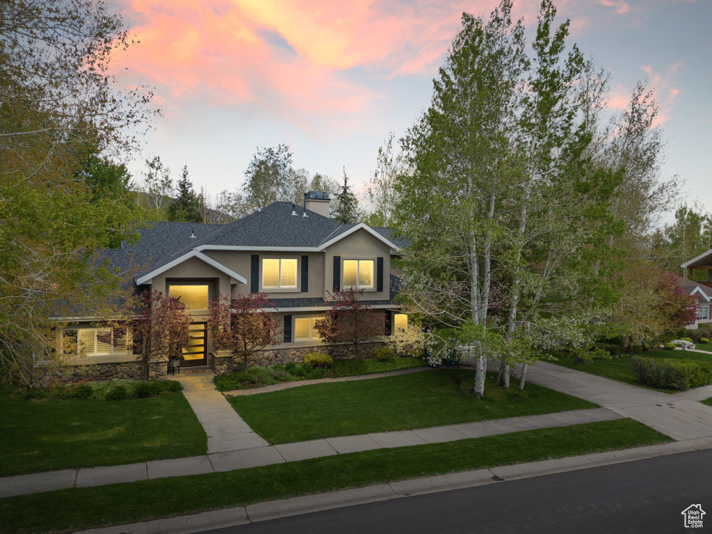 View of front of home featuring stone siding, stucco siding, a lawn, and a chimney