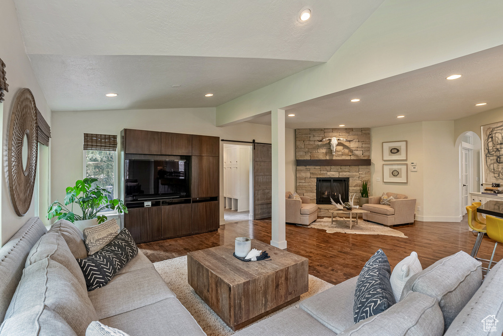 Living area with vaulted ceiling, arched walkways, wood finished floors, recessed lighting, and a stone fireplace