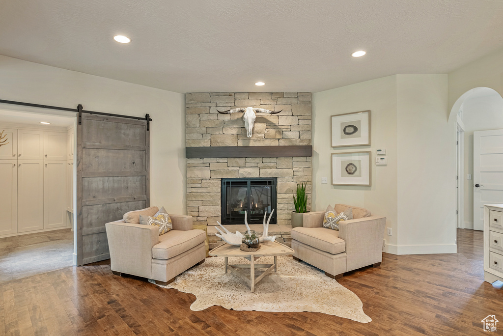 Living room featuring arched walkways, a barn door, dark wood-style floors, a fireplace, and recessed lighting
