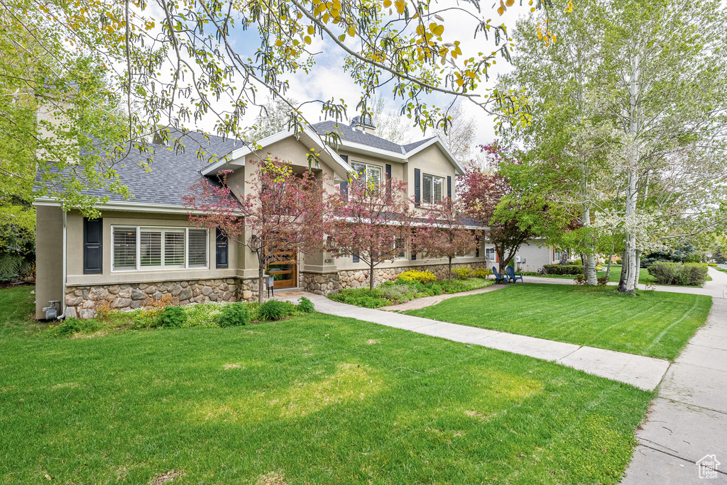View of front facade with stone siding, stucco siding, a shingled roof, and a front yard
