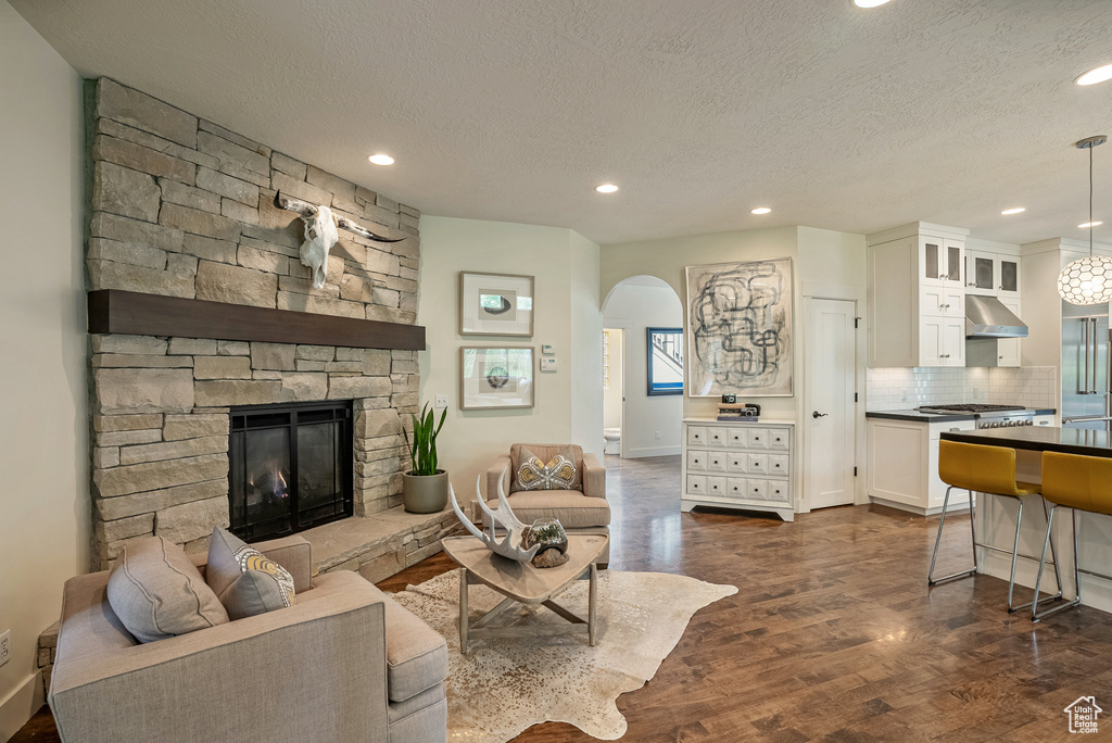 Living room featuring recessed lighting, arched walkways, a stone fireplace, a textured ceiling, and dark wood-style flooring