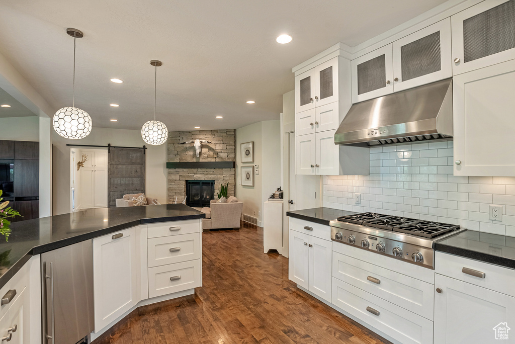Kitchen with under cabinet range hood, stainless steel gas stovetop, a barn door, dark countertops, and recessed lighting