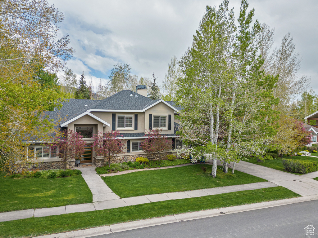 View of front of home with a front lawn, stone siding, a chimney, and stucco siding