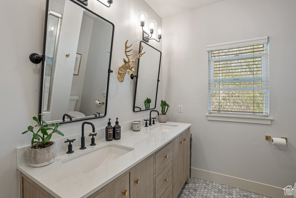 Full bathroom featuring toilet, double vanity, plenty of natural light, and tile patterned flooring