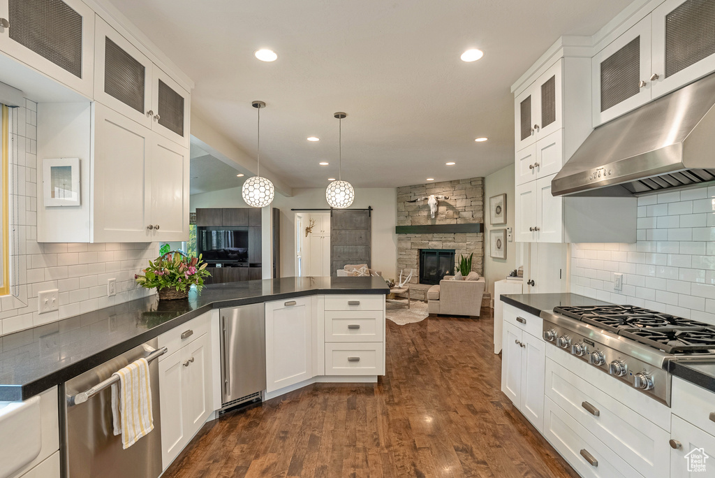 Kitchen featuring stainless steel appliances, range hood, open floor plan, dark countertops, and recessed lighting
